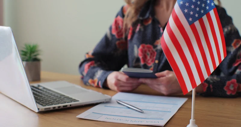 mulher enviando aplicação para visto com bandeirinha dos estados unidos na frente do computador braztrip agência de viagens